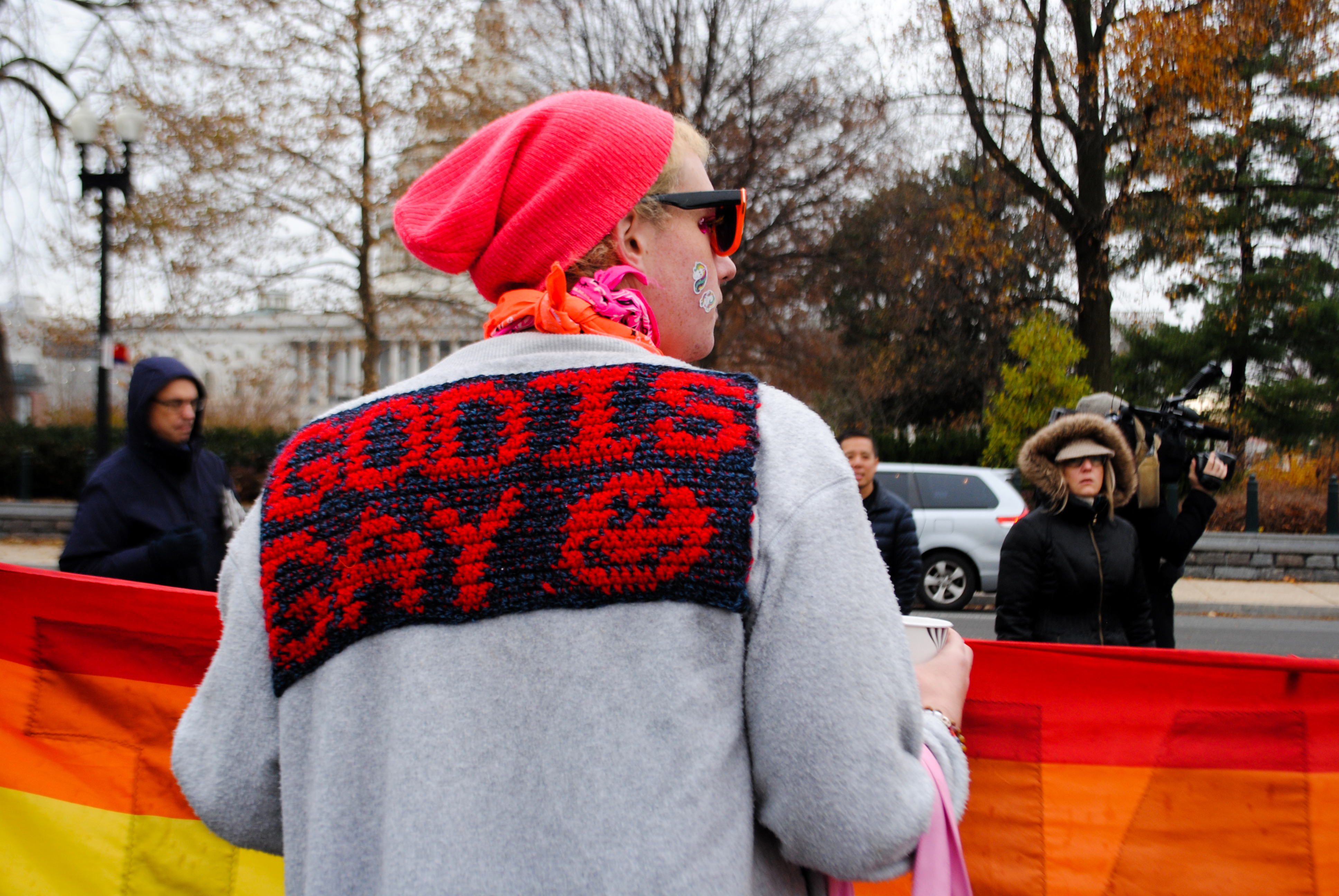 A protestor, back towards the camera, has knitted into the back of their sweater: God is Gay