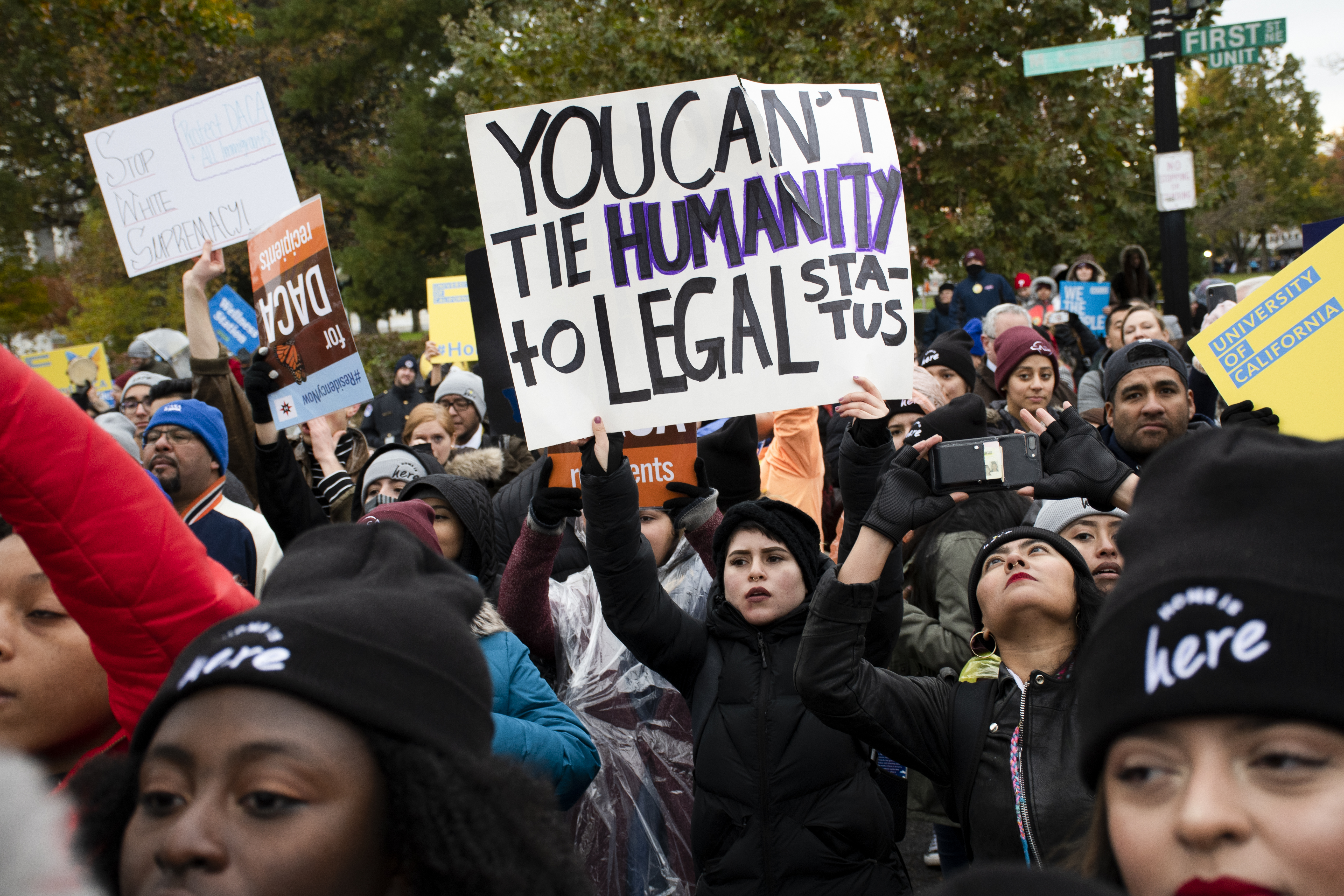 A woman among a crowd of protestors holds up sign that reads: You can't tie humanity to legal status