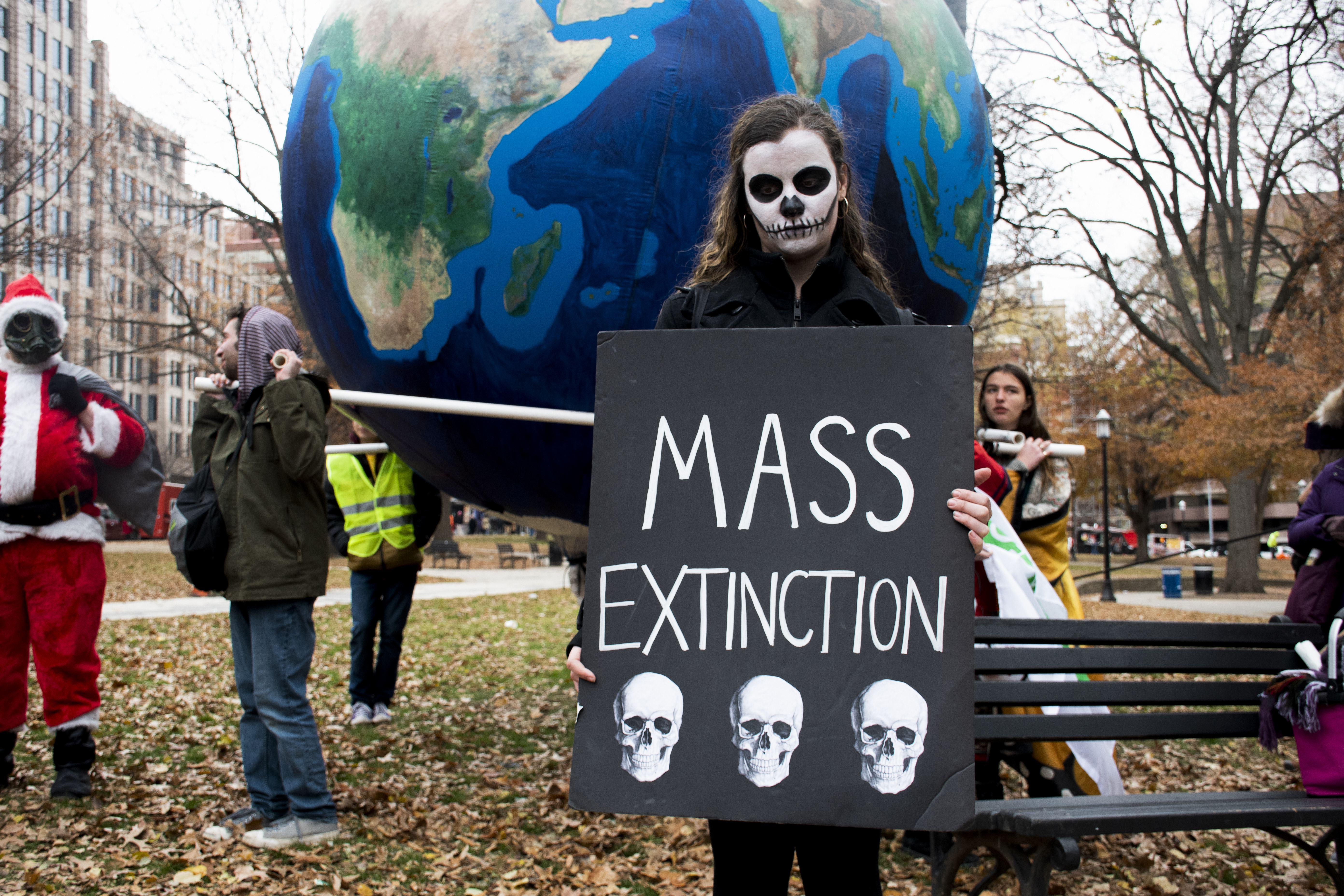 A woman, her face painted like a skeleton, stands in front of a giant inflated Earth with a sign that reads: Mass Extinction