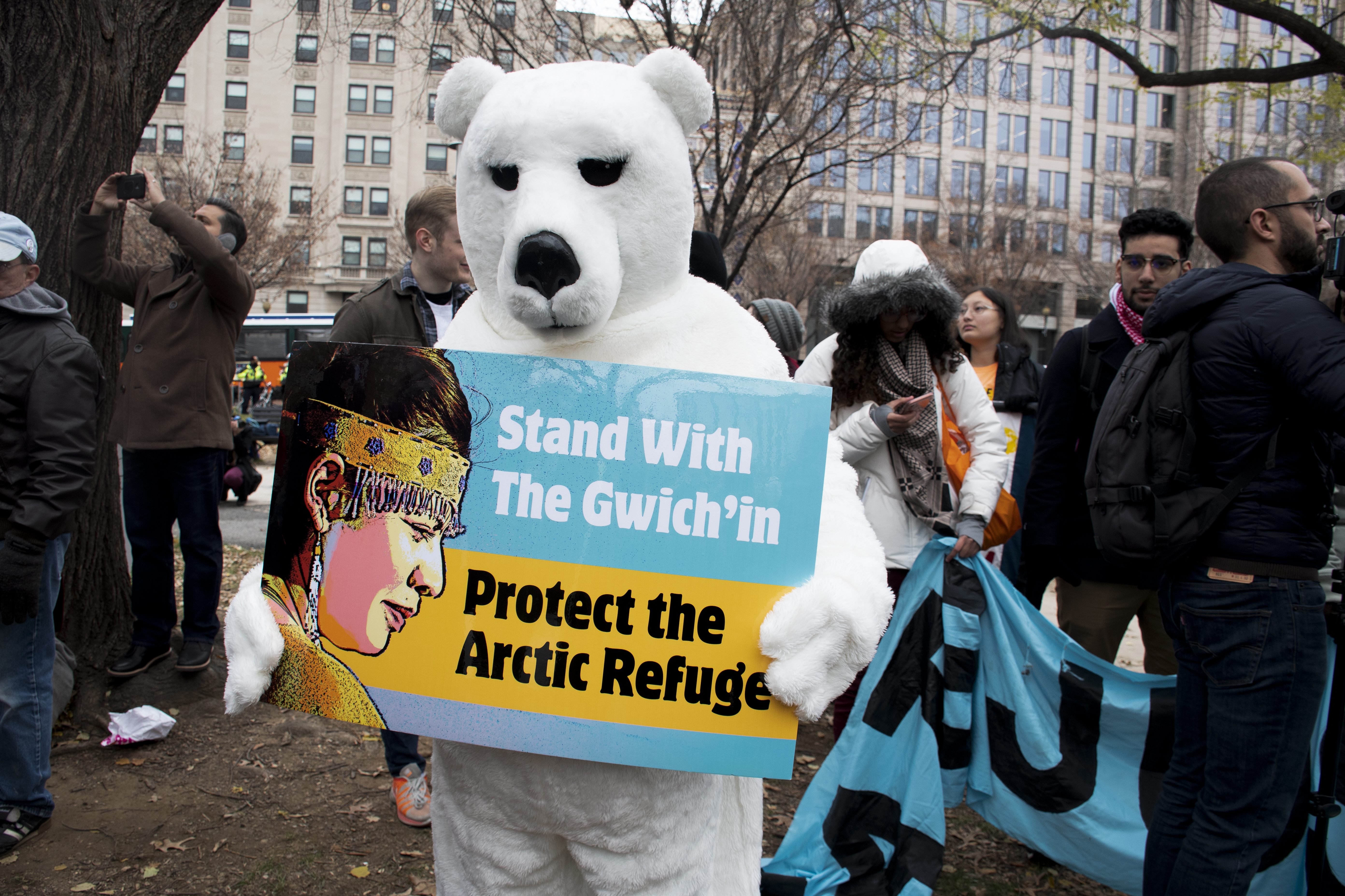 A protestor in a polar bear costume holds up a sign that says: Stand with the Gwich'in. Protect the Arctic Refuge