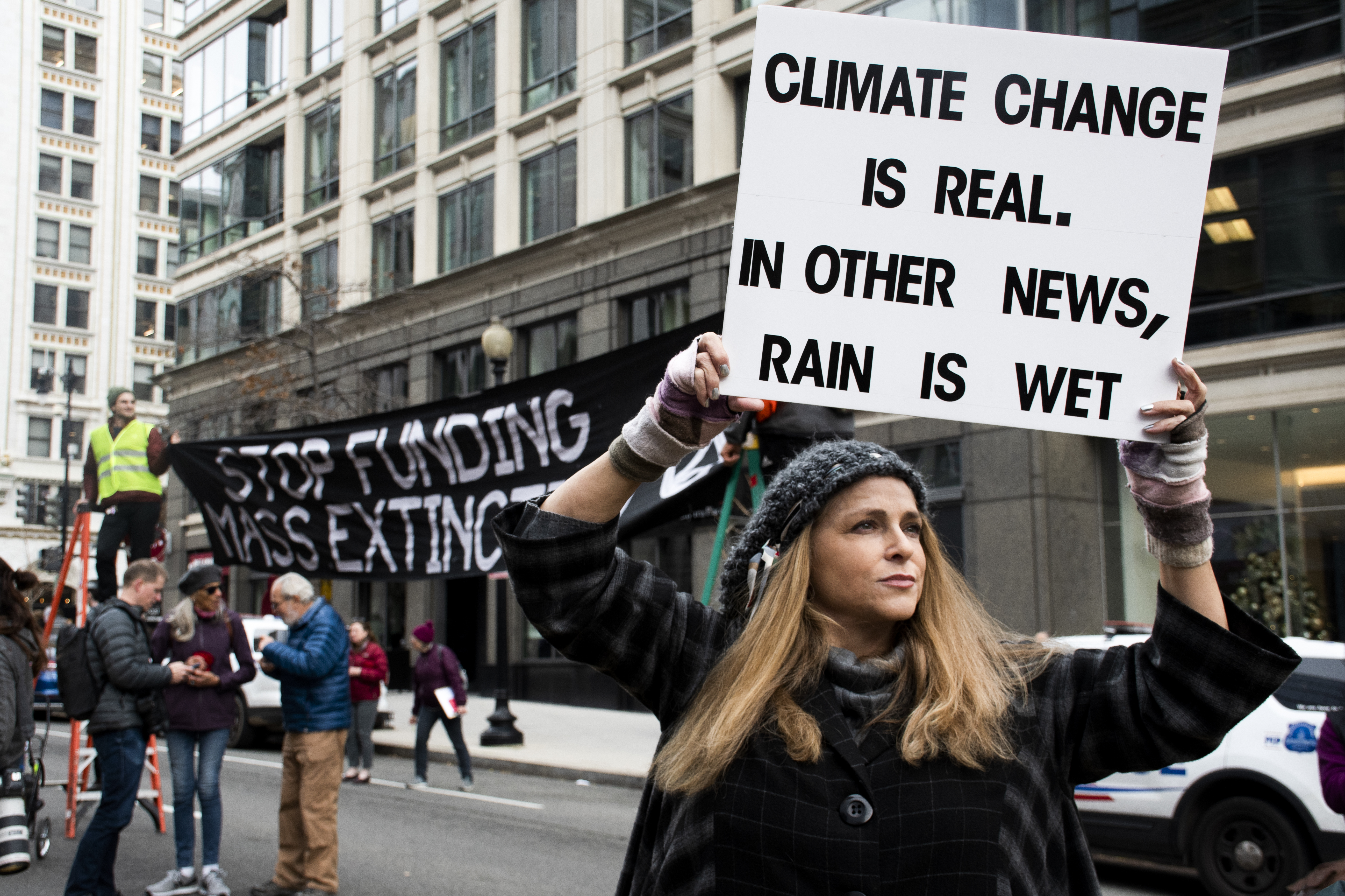 Woman with sign that reads: Climate change is real. In other news, rain is wet.