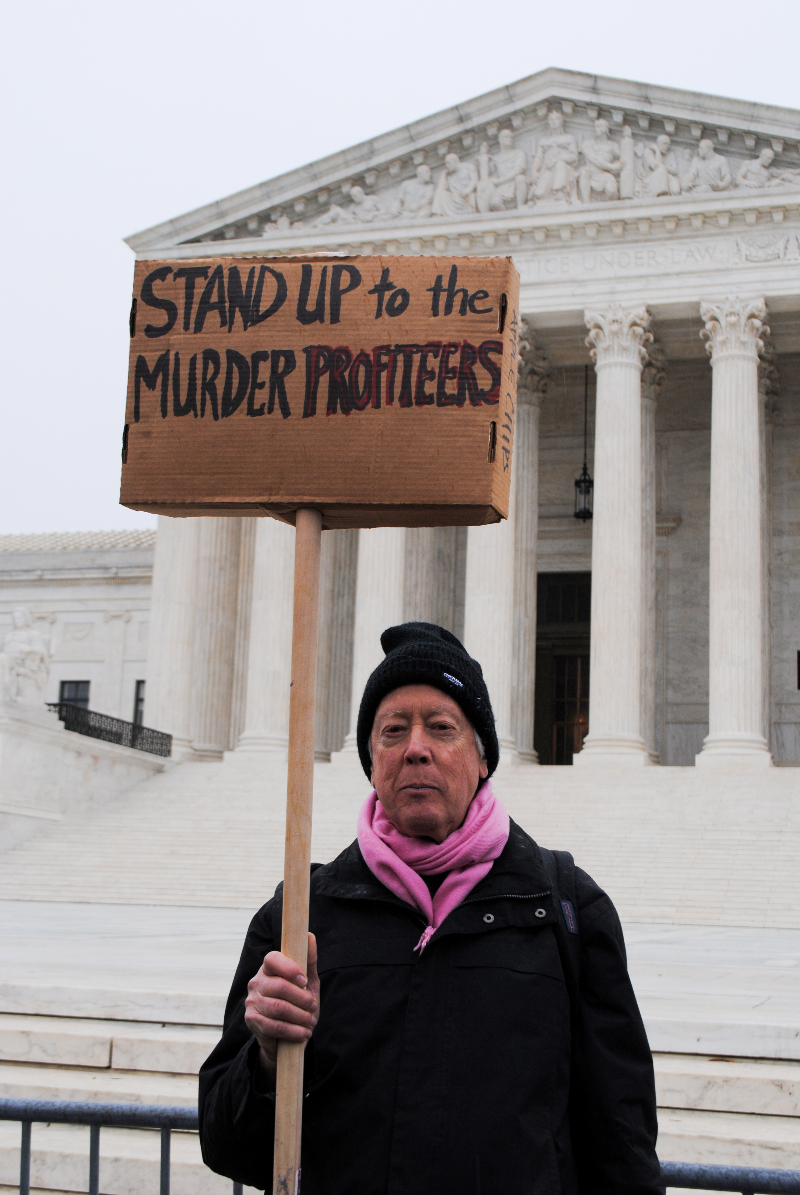 Man in front of Supreme Court with sign that reads: Stand up to the murder profiteers.