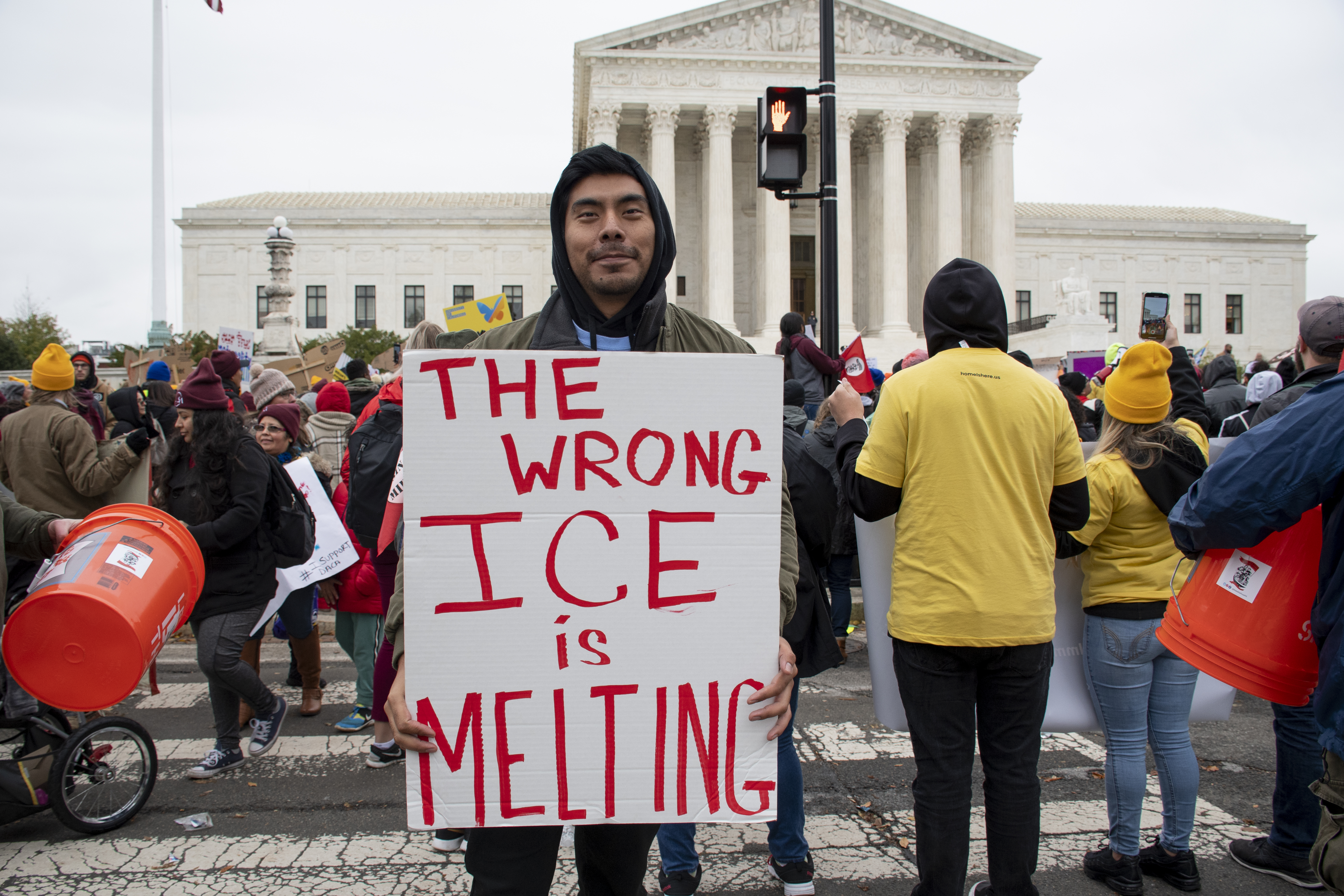 A man in front of crowds in front of the Supreme Court holds up sign that says: The wrong ICE is melting